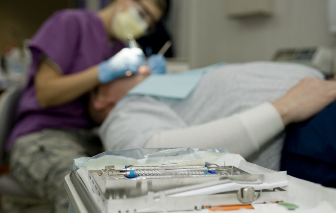 A table covered in dental equipment and supplies sits in the foreground of a military dental procedure in progress.