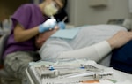 A table covered in dental equipment and supplies sits in the foreground of a military dental procedure in progress.