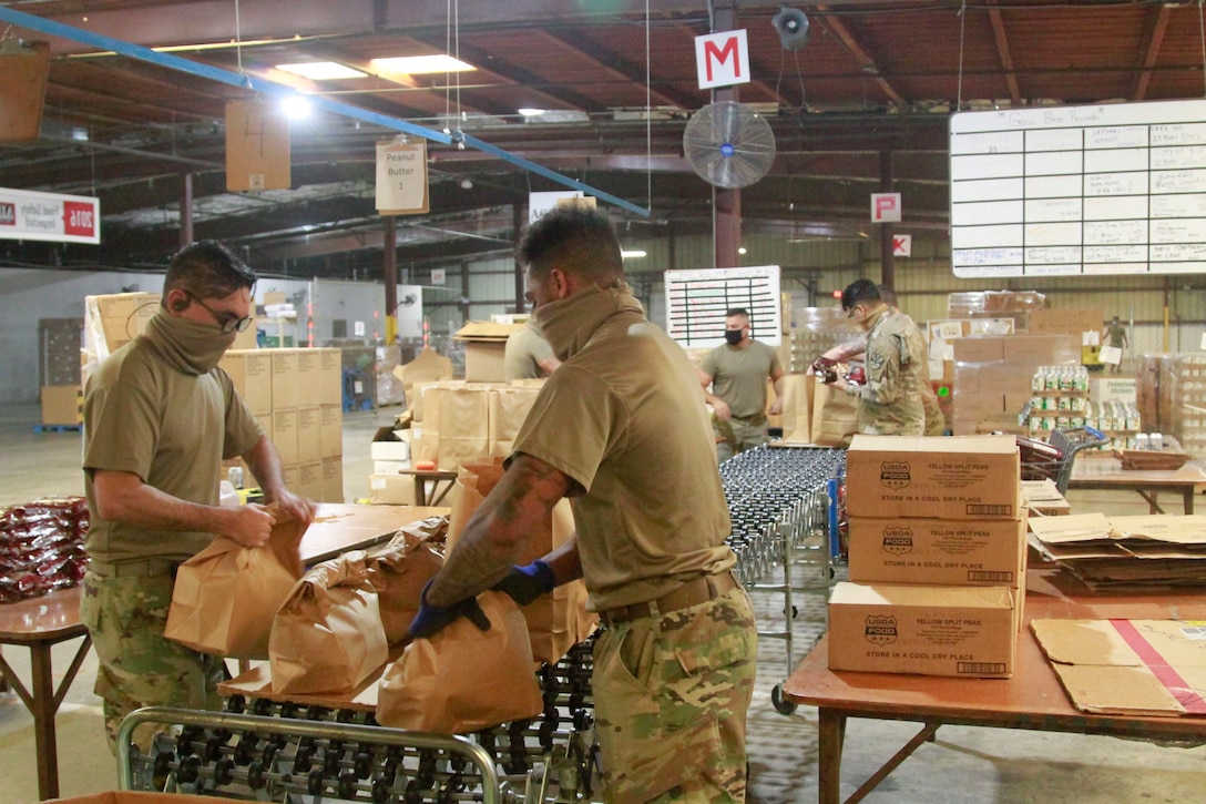 Soldiers put food in grocery bags at a warehouse.