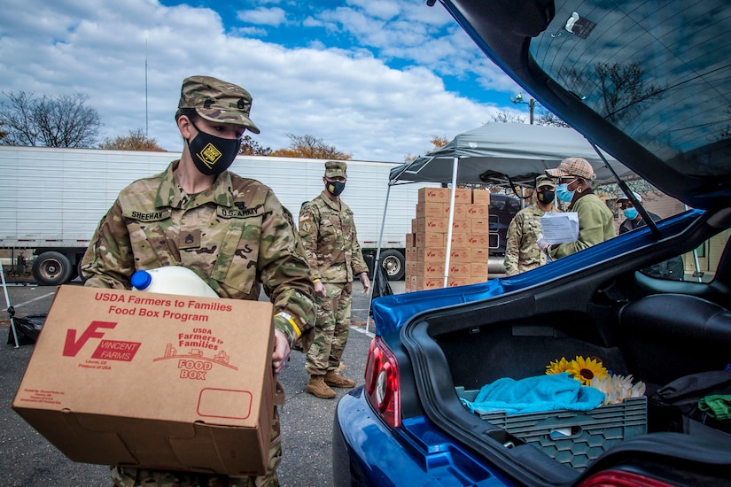 A soldier carries a box of food to the trunk of a car.