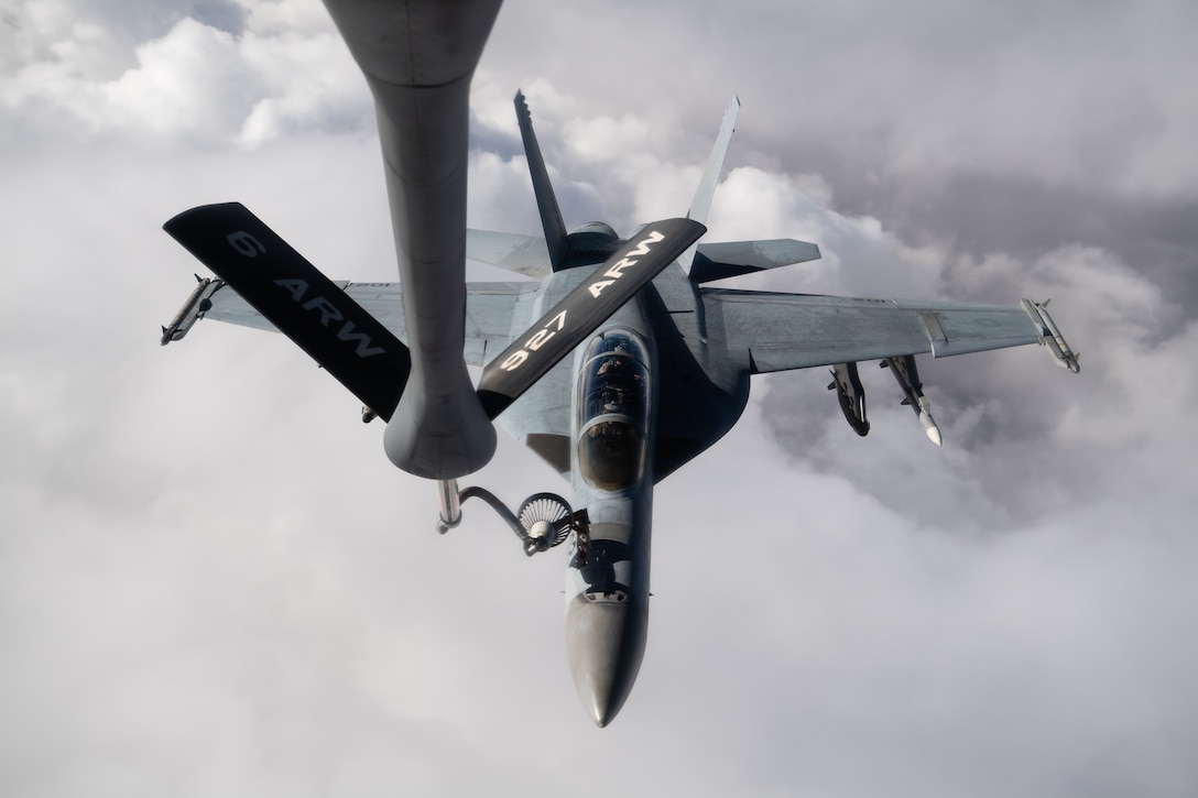 A long pole carrying fuel from a tanker aircraft attaches to a fighter jet while flying in clouds.