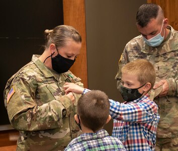 Newly promoted Sgt. 1st Class Lindsey Gibbs’ sons, Owen and Henry, place her new rank on her uniform as husband, CWO3 Brandon Gibbs places her new rank on her cap during her promotion ceremony at the Illinois Military Academy, Camp Lincoln, Springfield, Illinois Oct. 15.