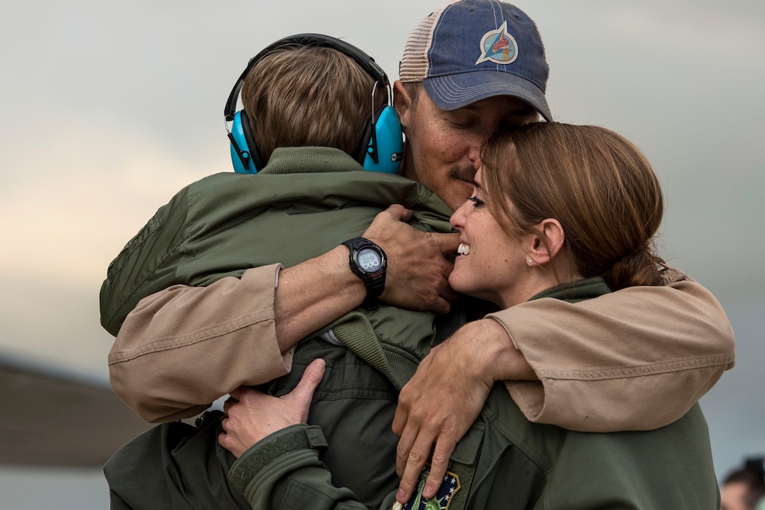 An airman smiles while embracing one adult and one child.