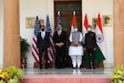 Four men wearing masks pose for a photo in front of the U.S. and Indian flags.
