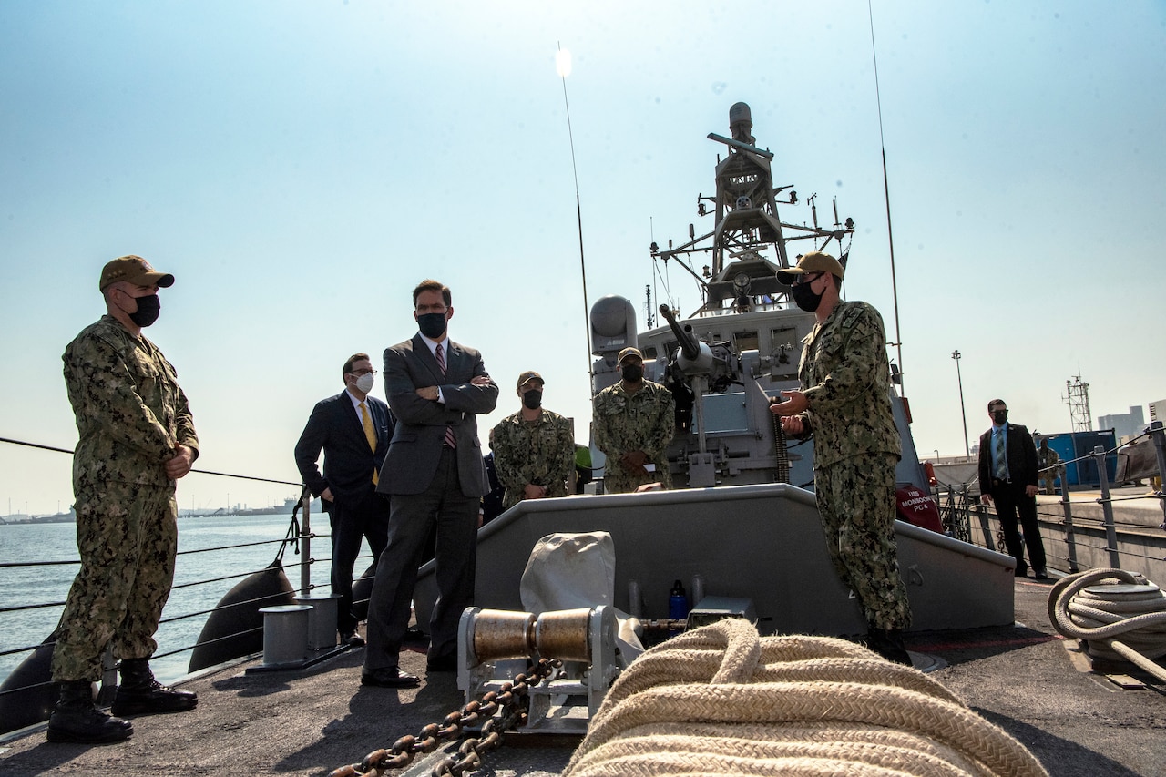 Defense Secretary Dr. Mark T. Esper stands on a ship with service members.