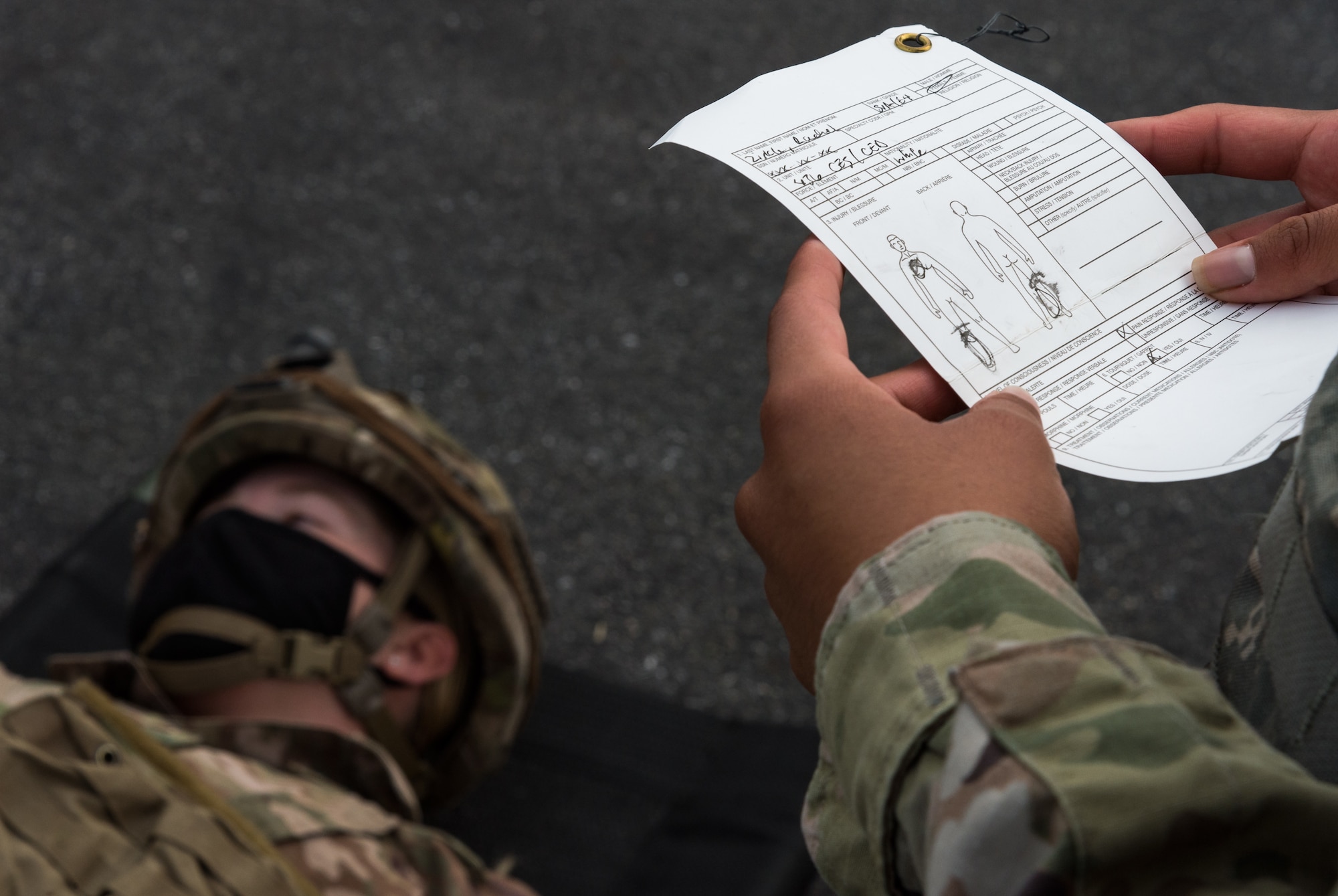 As part of a self-aid and buddy care training exercise, a 436th Civil Engineer Squadron Prime Base Engineer Emergency Force member reviews a tactical combat casualty care card identifying simulated injuries to Senior Airman Rachel Zirkle, 436th CES explosive ordnance disposal journeyman, Oct. 21, 2020, on Dover Air Force Base, Delaware. Sixty-four Prime BEEF members made up 10 teams in a 96-hour readiness exercise that included SABC, vehicle convoy techniques and land navigation exercises prior to arriving at the Tactics and Leadership Nexus. While at the TALN, they participated in night vision goggle familiarization; chemical, biological and radiological and nuclear defense training; individual movement techniques; and defense fighting position exercises. (U.S. Air Force photo by Roland Balik)