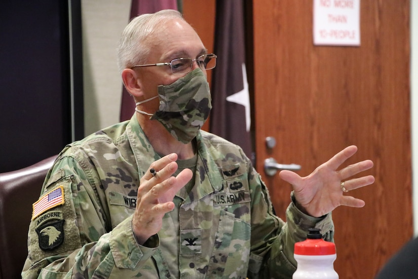 A man in a uniform and a face mask gestures while speaking.