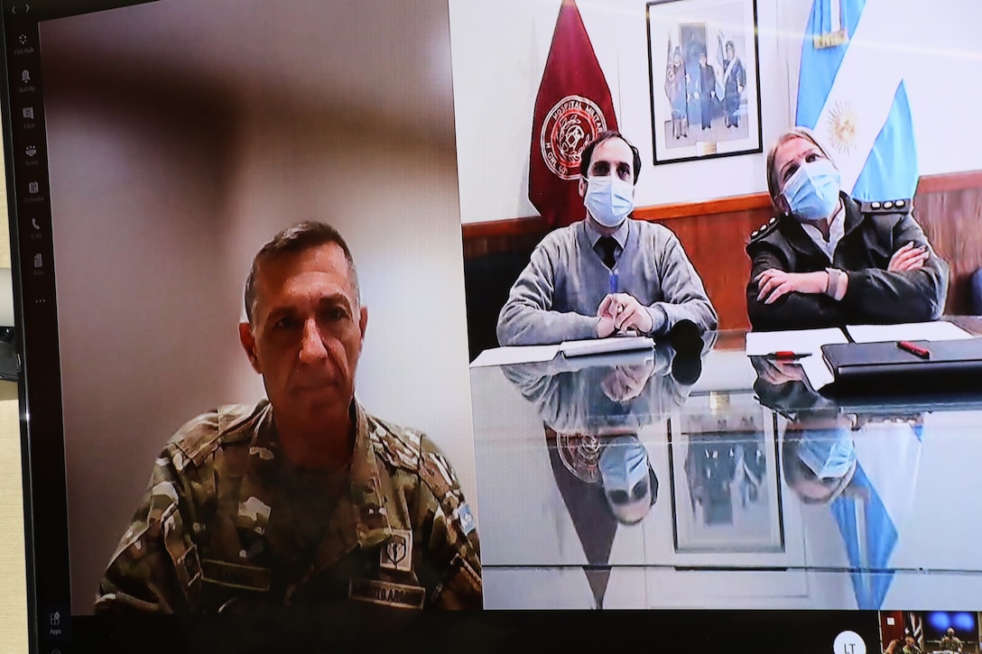 A man in a military uniform is shown on the left side of the picture and a civilian and an officer from a foreign country are shown on the screen to his left.