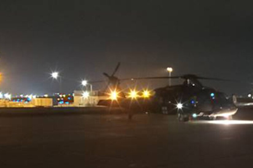 A helicopter sits on the tarmac at night.