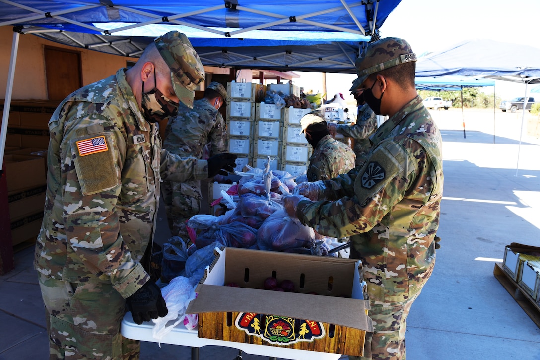 Several national guardsmen wearing face masks and gloves prepare boxes of groceries for delivery to residents.