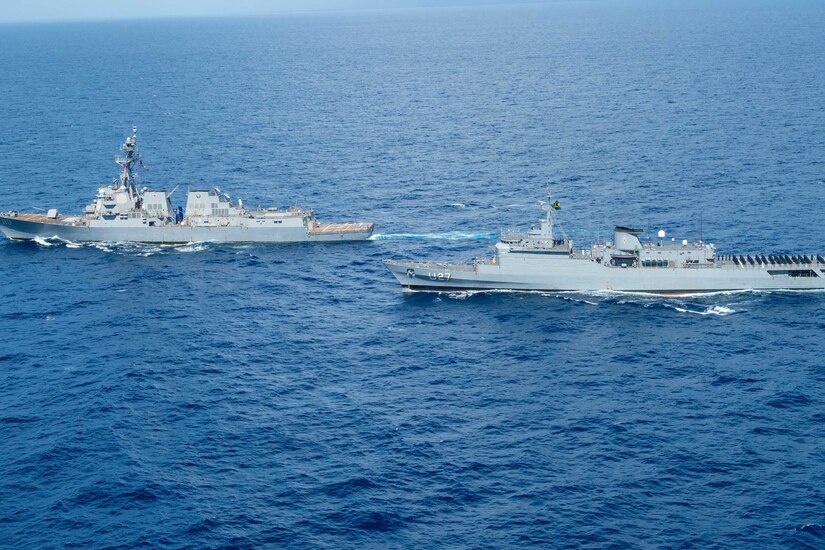 Two military ships steam together in the ocean.