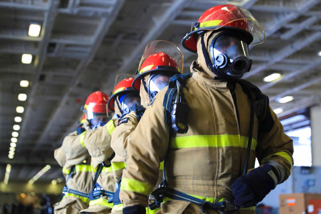 Sailors wearing fire protection gear stand in a line.