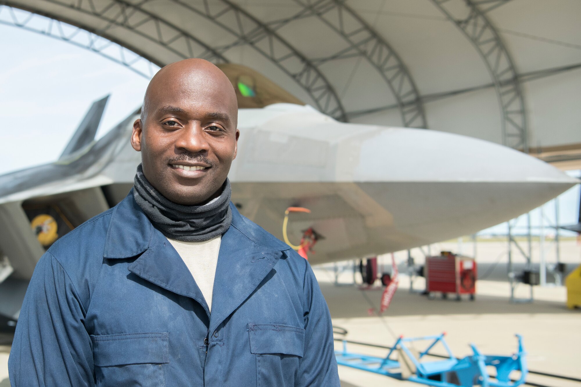 A man wearing blue coveralls smiles for a portrait in front of a jet