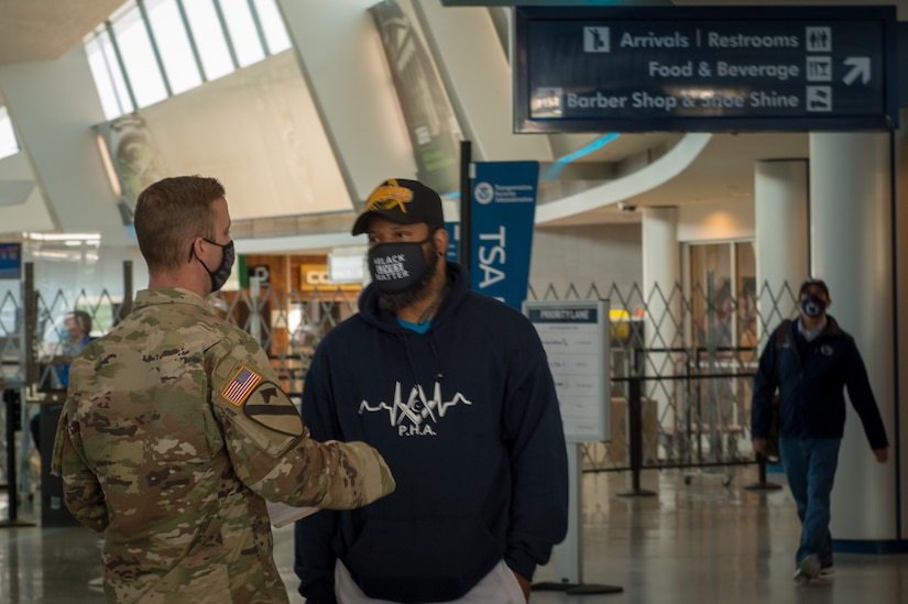 A service member talks to a man in civilian clothing in an airport.