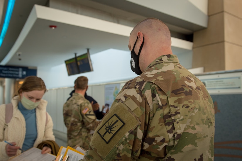 A service member watches a woman fill out a form at an airport.