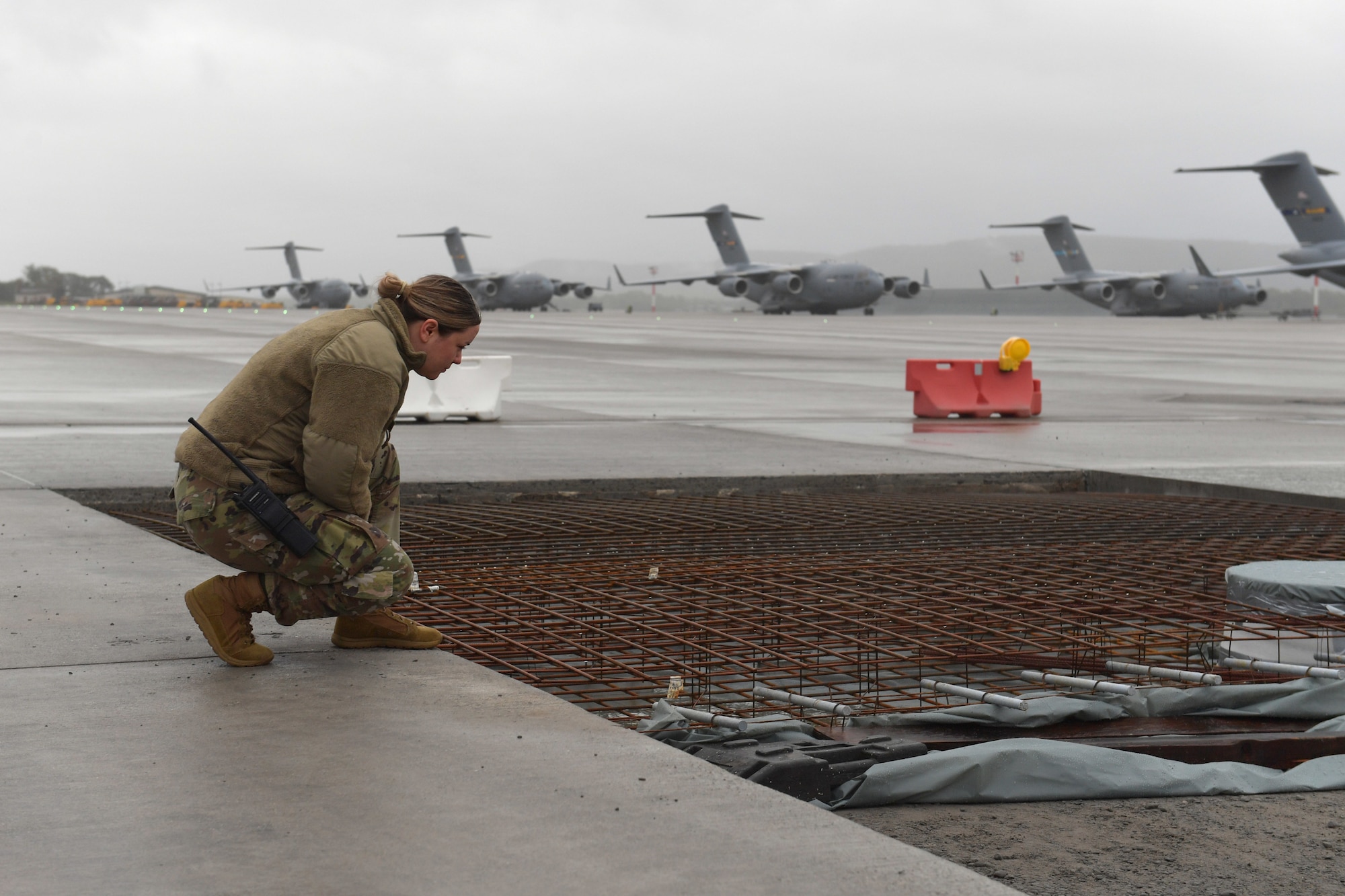An Airman kneeling beside a construction site on an airfield.