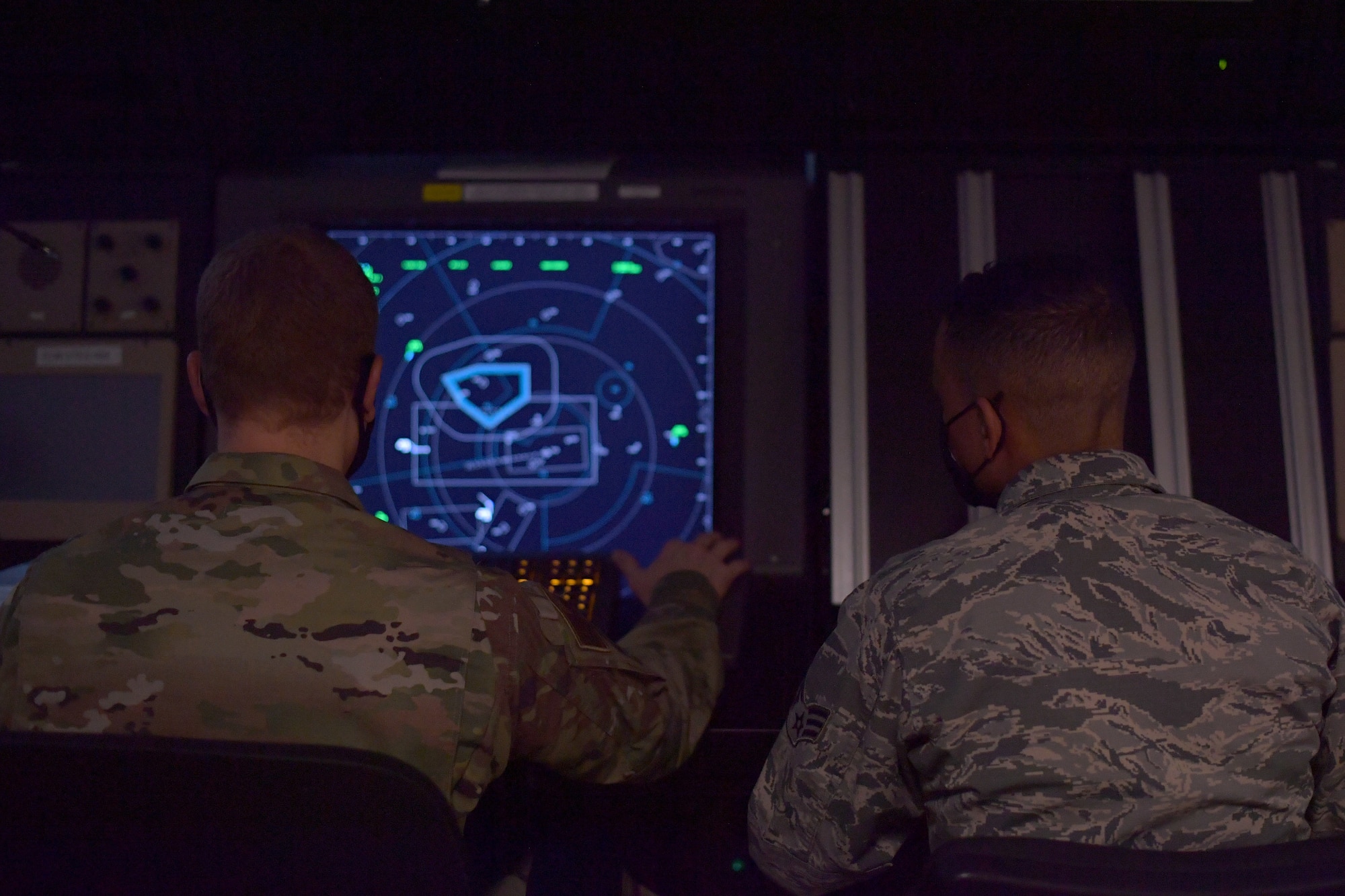 Two Airmen sit in front of a radar screen.