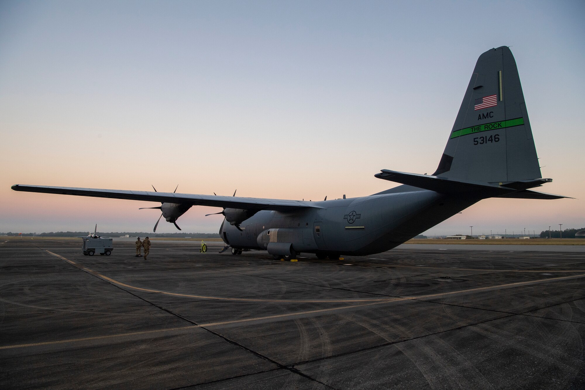 A C-130J sits on the runway at sunrise.