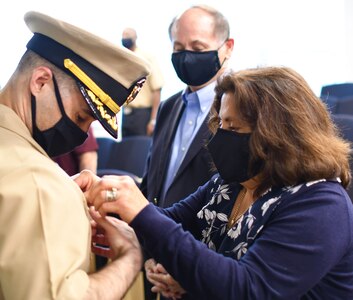 IMAGE: VIRGINIA BEACH, Va. (Oct. 16, 2020) – Cmdr. Michael Aiena, commanding officer of Naval Surface Warfare Center Dahlgren Division (NSWCDD) Dam Neck Activity, receives his command ashore pin from his mother while his father looks on at a change of command ceremony held at Dam Neck Activity’s Hopper Hall auditorium. Aiena relieved Cmdr. Joe Oravec during the ceremony. “My parents are the reason I’m here,” said Aiena, who told the audience on site and over a live Teams broadcast that he is humbled to assume command at NSWCDD Dam Neck Activity. “I am thrilled with this opportunity to work with the Sailors and civilians that make up the command for they are our most valuable resource.”  (U.S. Navy photo/Released)