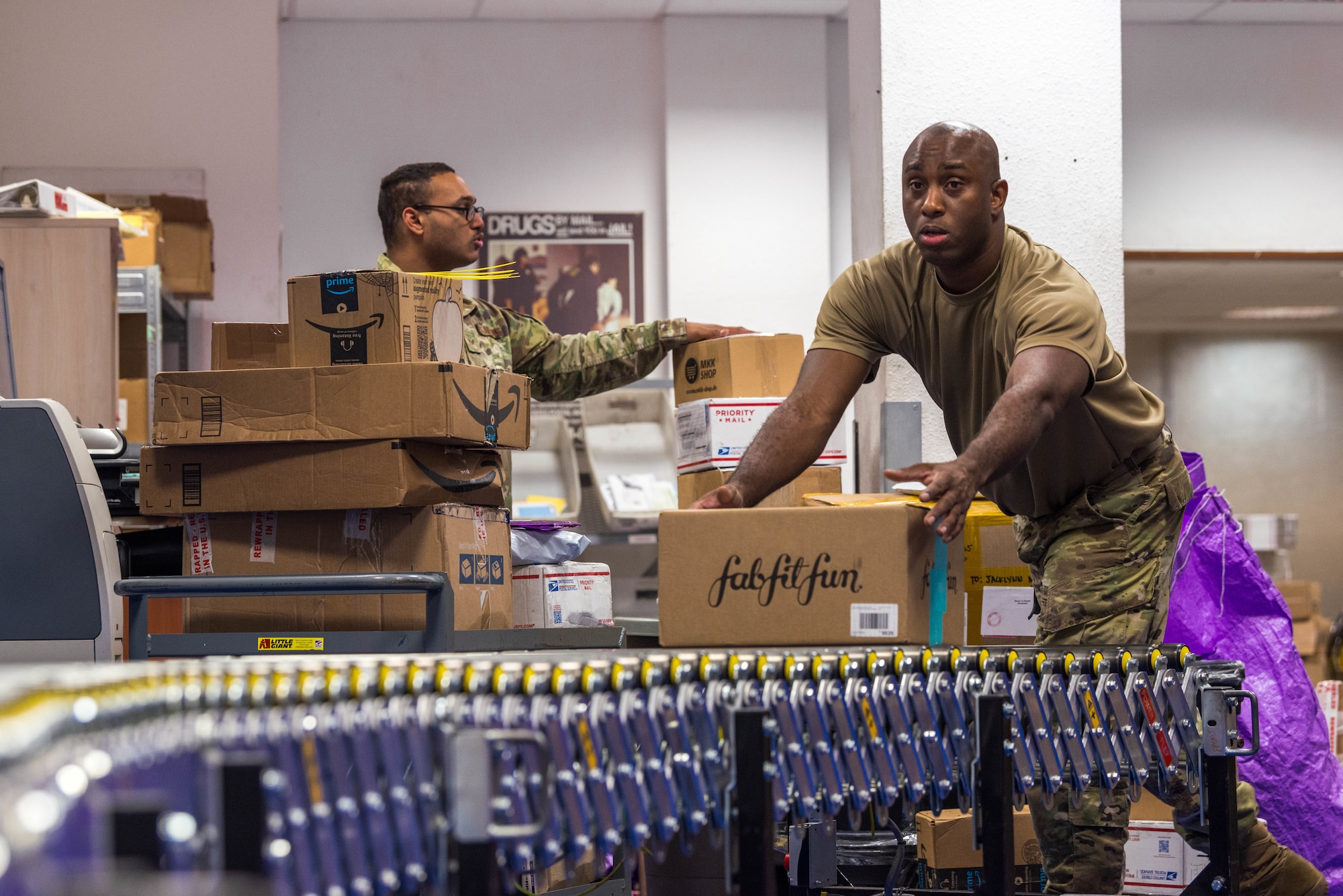 U.S. Air Force Staff Sgt. Kamar Francis, 786th Force Support Squadron postal service center noncommissioned officer in charge, grabs a package off of a roll-out conveyor belt at Ramstein Air Base, Germany, Oct. 27, 2020. Two roll-out conveyor belts that extend to both sides of the Northside Post Office are used in conjunction with a stationary conveyor belt to accelerate processing incoming packages. (U.S. Air Force photo by Senior Airman Noah Coger)