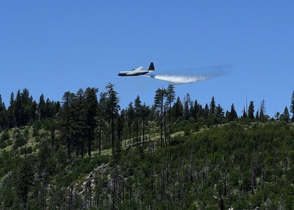 About 150 feet above a tree line, a California Air National Guard C-130 aircraft releases 3,000 gallons of water, covering nearly a quarter mile, during aerial wild land firefighting training June 15-19, 2020, at the Tahoe National Forest.