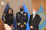 Three people wearing masks stand in front of military flags