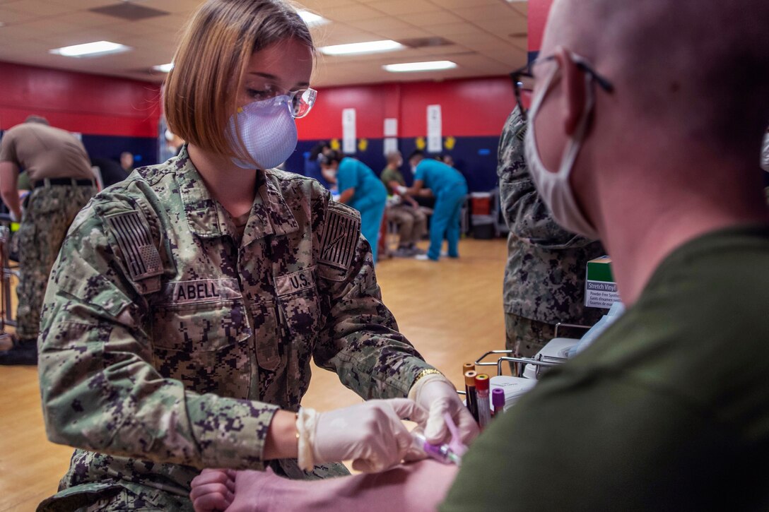 A sailor wearing a face mask and gloves draws blood from a sailor.