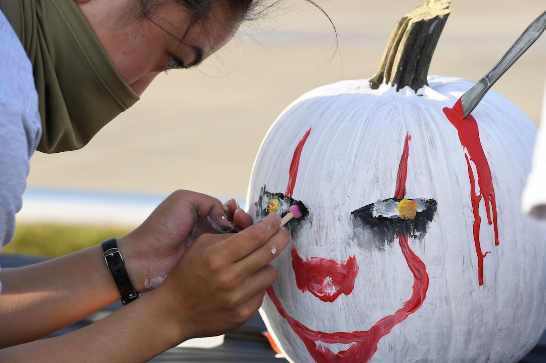 An airman wearing a face mask paints a pumpkin.