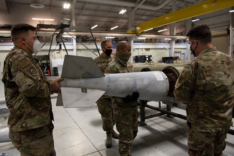 Two Airmen picks up and install a JDAM tail kit to a BLU-109 bomb body.