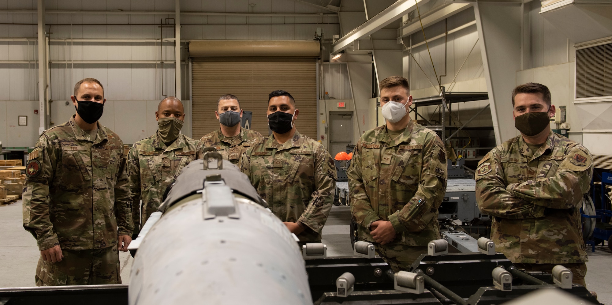 A group of Airmen pose for a photo in front of a GBU.