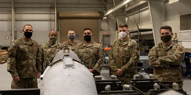 A group of Airmen pose for a photo in front of a GBU.
