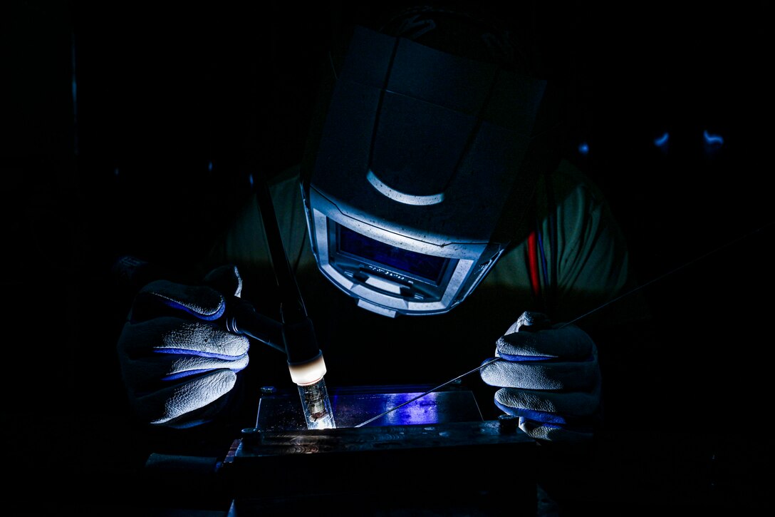 An airman in protective gear welds metal plates.