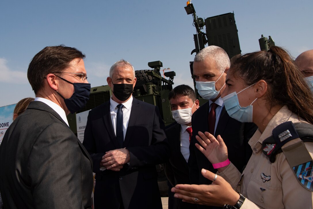 An Israeli military officer speaks to a group of people in suits wearing protective face masks.