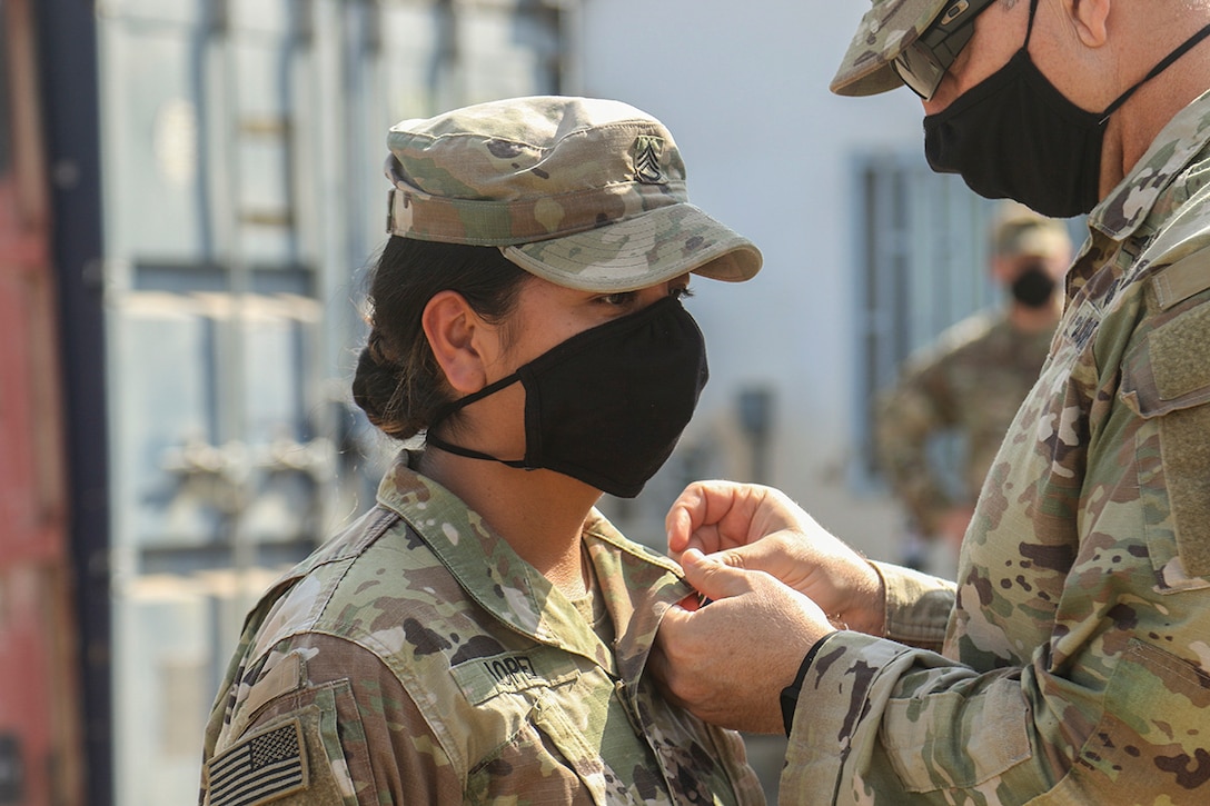 A soldier pins a medal on another soldier’s shirt collar.