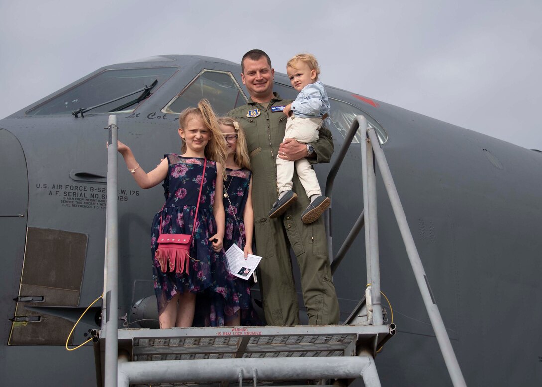 An Airmen stand with his two young girls in front of a B-52 while holding his son.