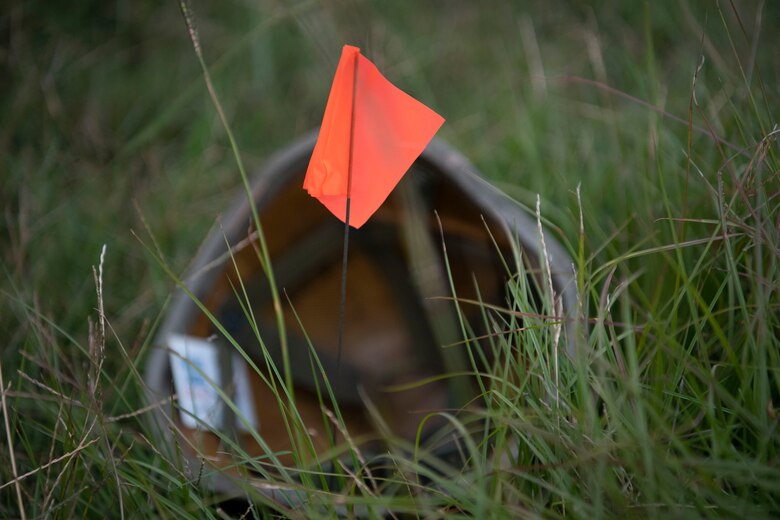 A kevlar helmet lays in the grass with a flag in front of it.