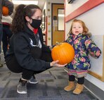 Staff Sgt. Megan Aycock, Colorado Springs Regional Command Post emergency actions controller, left, hands a pumpkin to her daughter Mabry, 1, as they prepare to leave the Child Development Center at Schriever Air Force Base Oct. 23, 2020. Parents picked up pumpkins to decorate for fun or to enter into the 50th Force Support Squadron’s pumpkin carving contest. (U.S. Space Force photo by Marcus Hill)