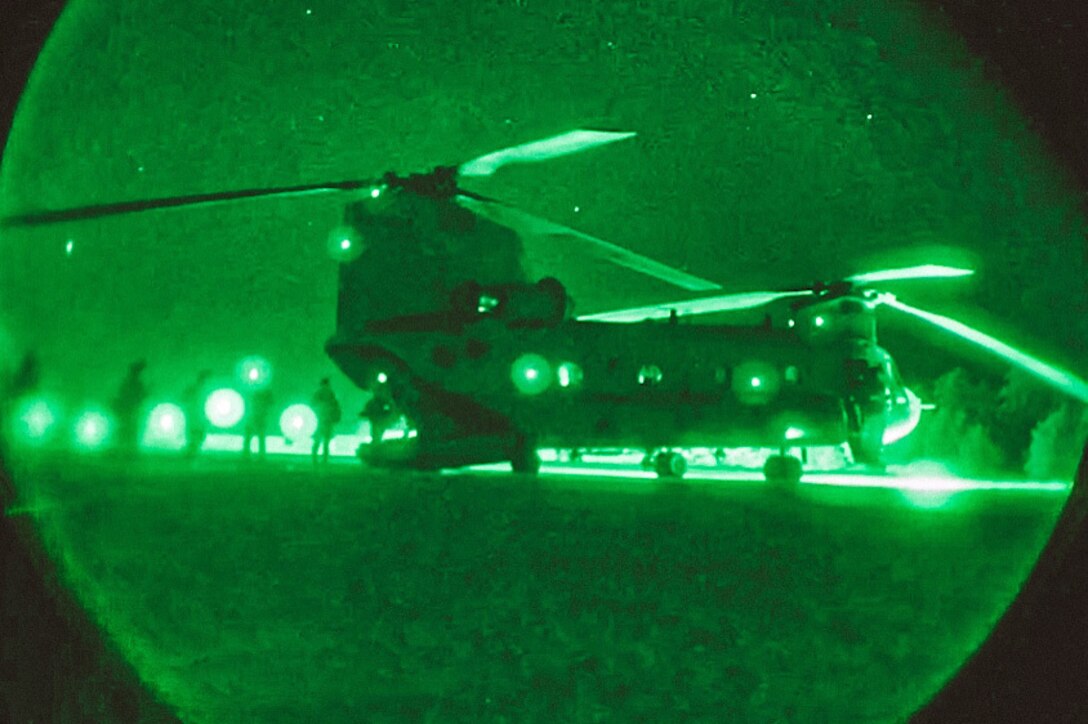 Soldiers load into a helicopter at night illuminated by green light.