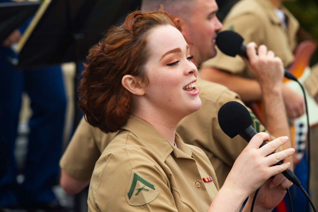 A Marine sings while other Marine perform in the background.