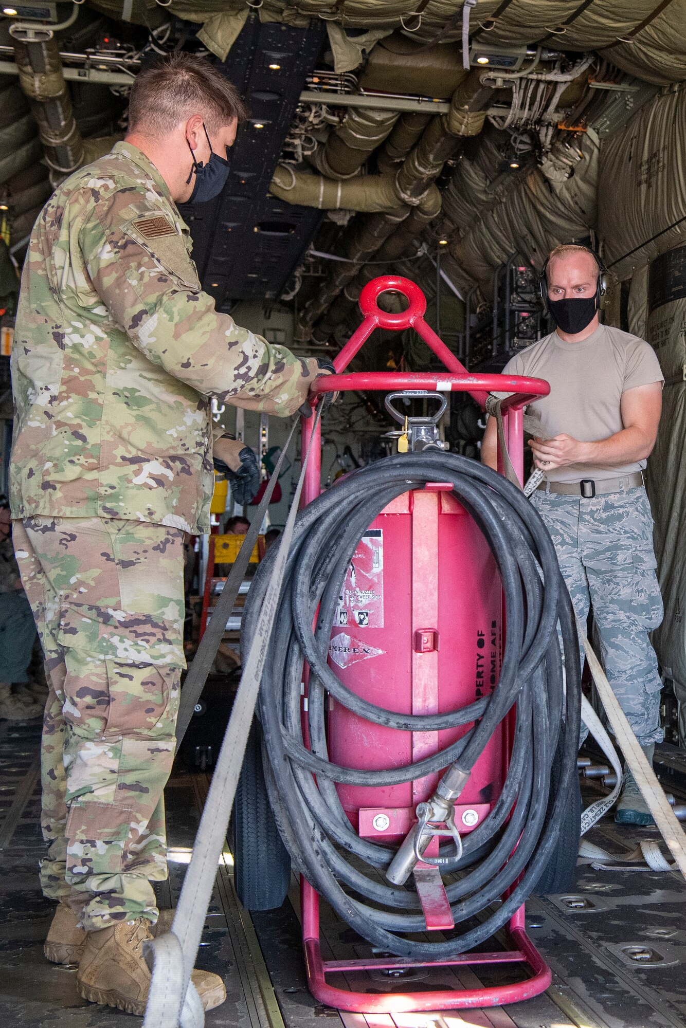 two Airmen tie down a fire bottle onto a C-130J Super Hercules.
