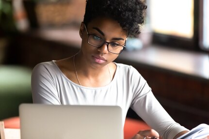 Thoughtful millennial African American woman in glasses look at laptop screen pondering