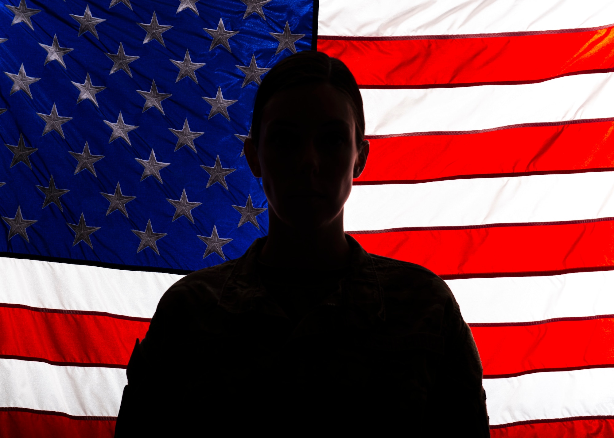 a silhouette of Senior Airman Zoe Wockenfuss stands in front of an illuminated American flag
