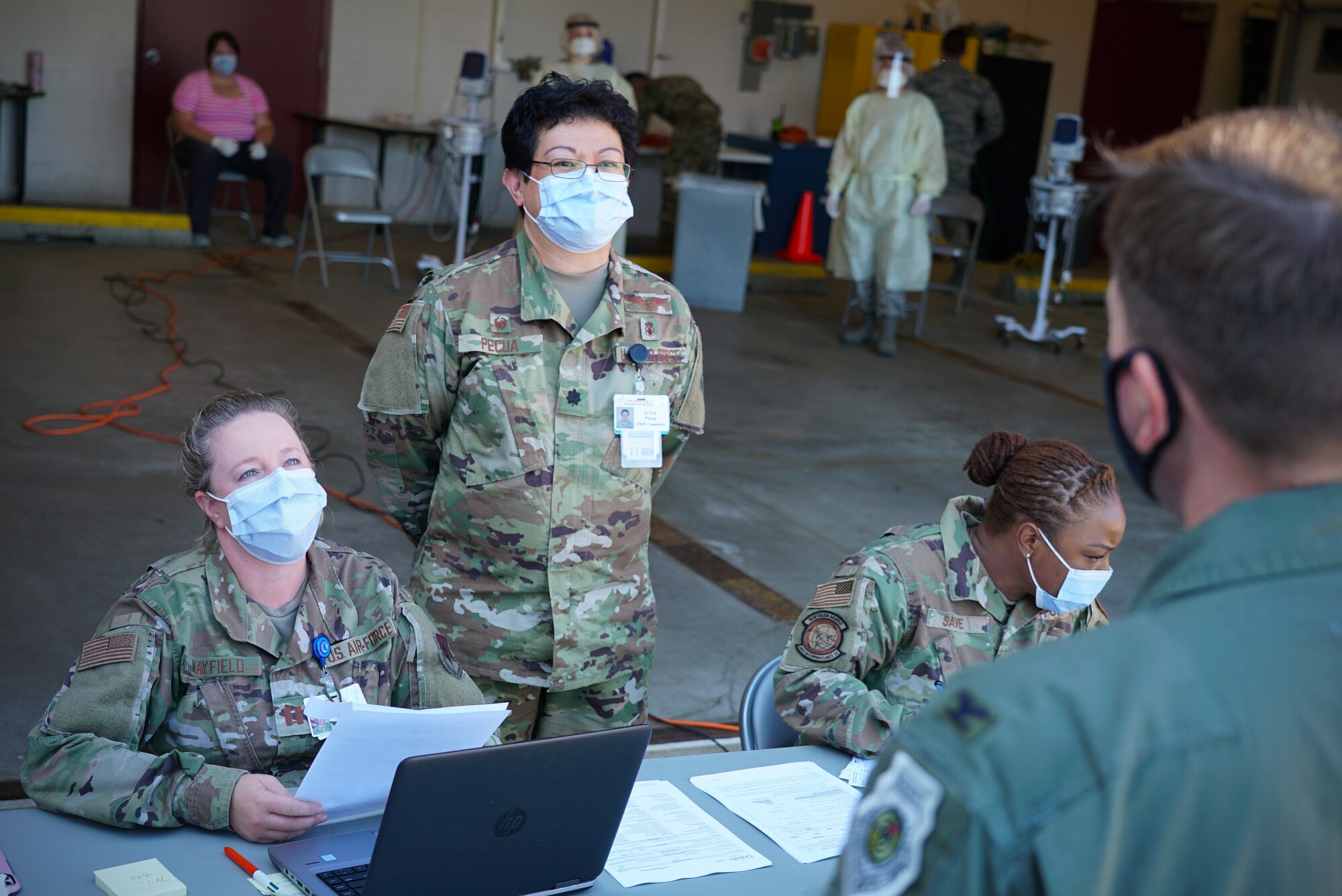 Two women in military uniform and face masks look at a patient as he checks in for an appointment.