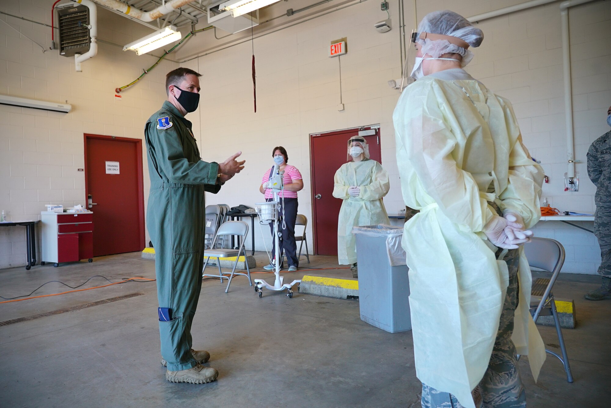 Man in flight suit looks at woman in medical protective gear as he talks.