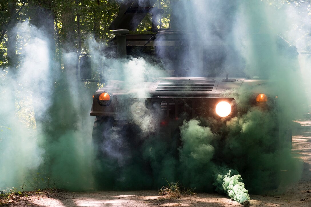A military vehicle drives through a cloud of green smoke in the forest.