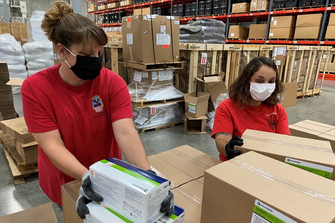 Two women pack boxes in a large warehouse.