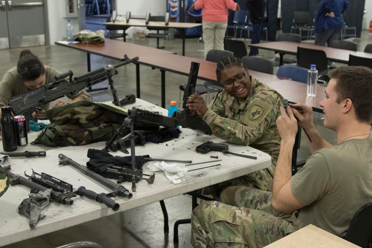 Three people in uniforms clean weapons.