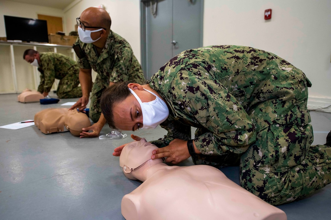 Sailors wearing masks perform CPR on mannequins.