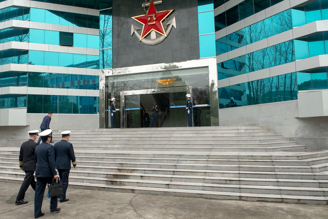 Men in military uniforms approach steps in front of a building.