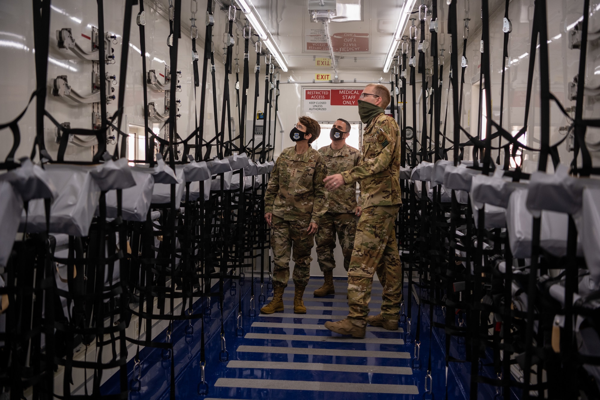 Three military members walk along a hallway with hanging seats